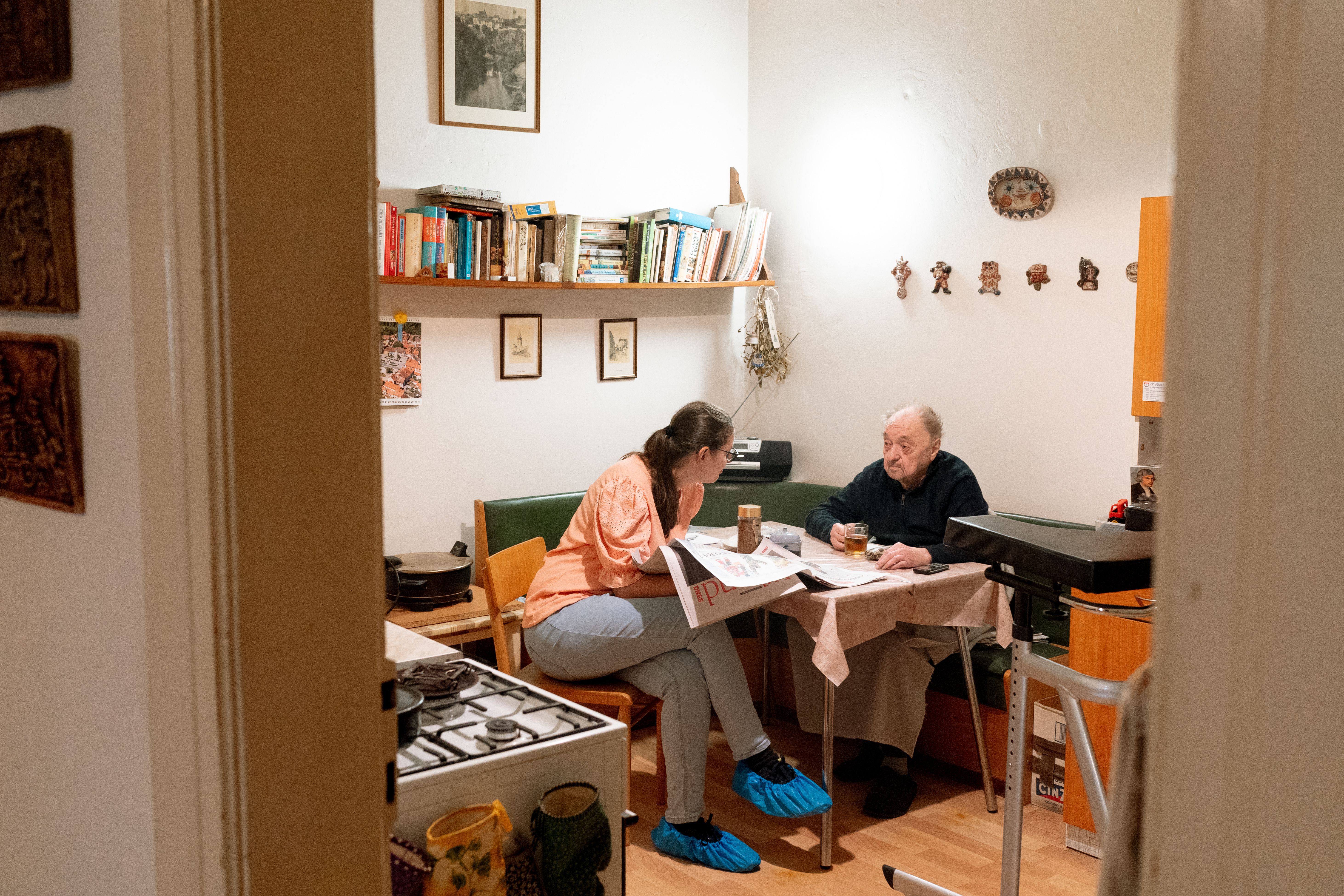 A caregiver and an older adult talk over coffee in a relaxed home setting.