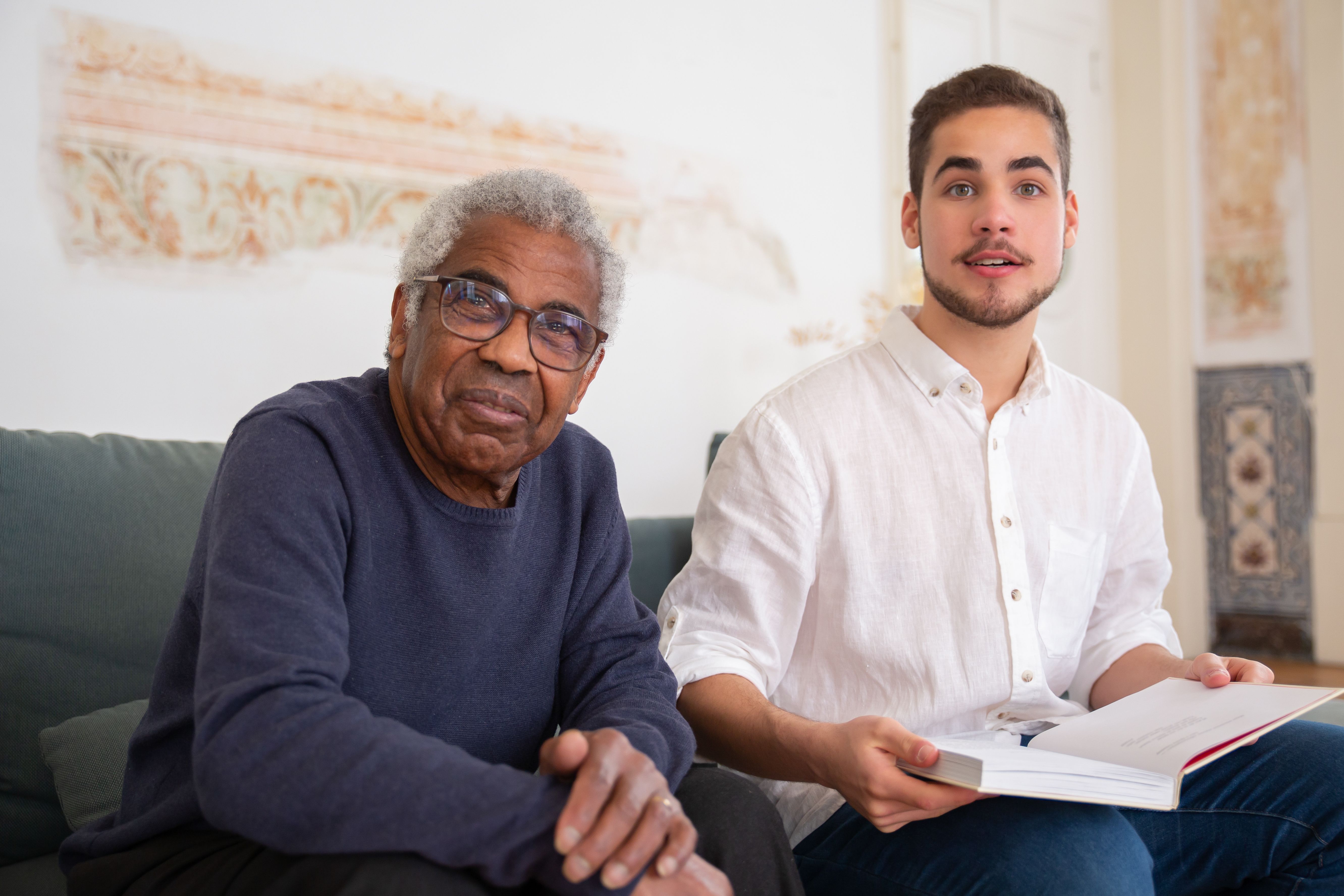 An older man and a young volunteer share a quiet moment reading together indoors.