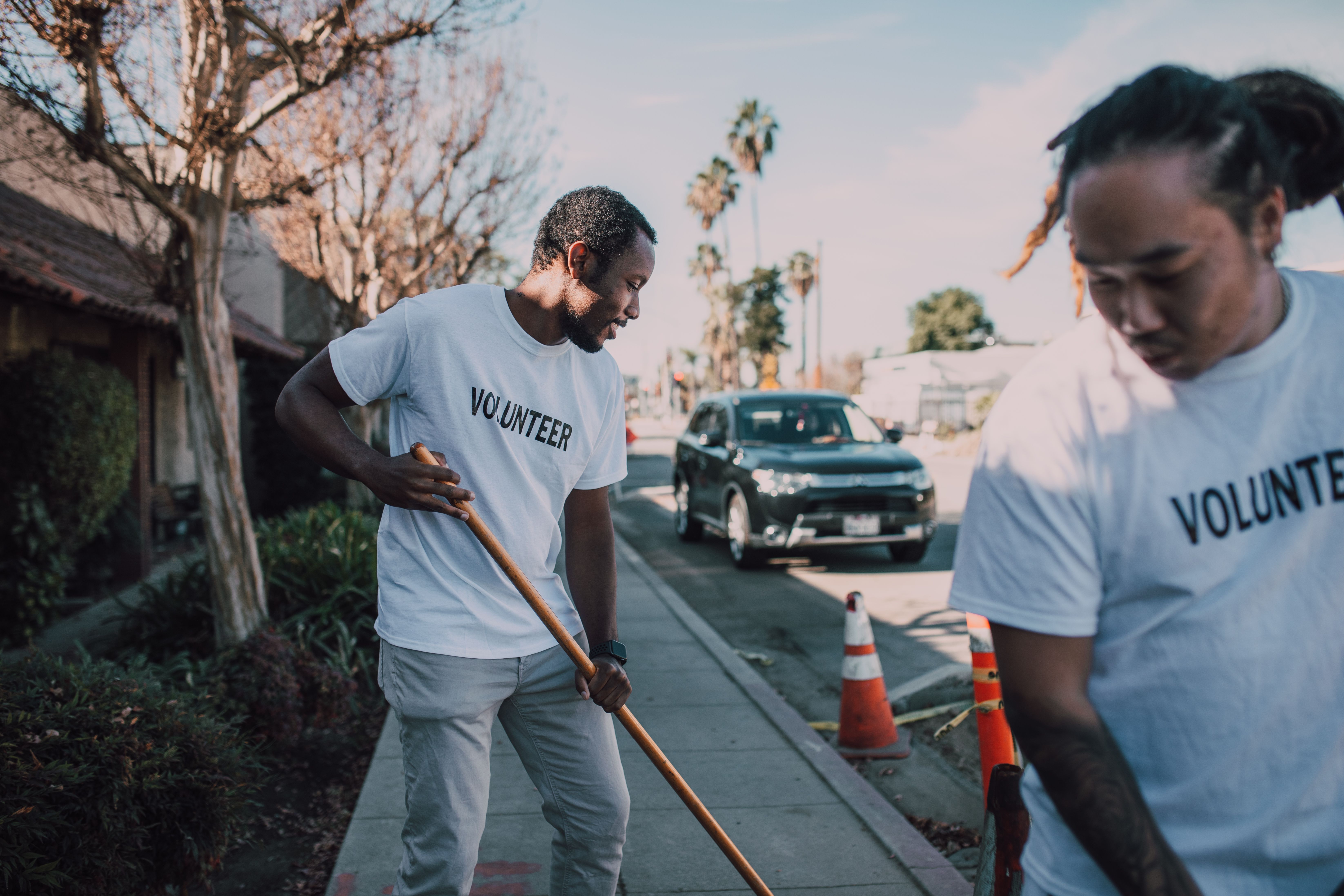 Two volunteers working together to clean a sidewalk on a sunny day